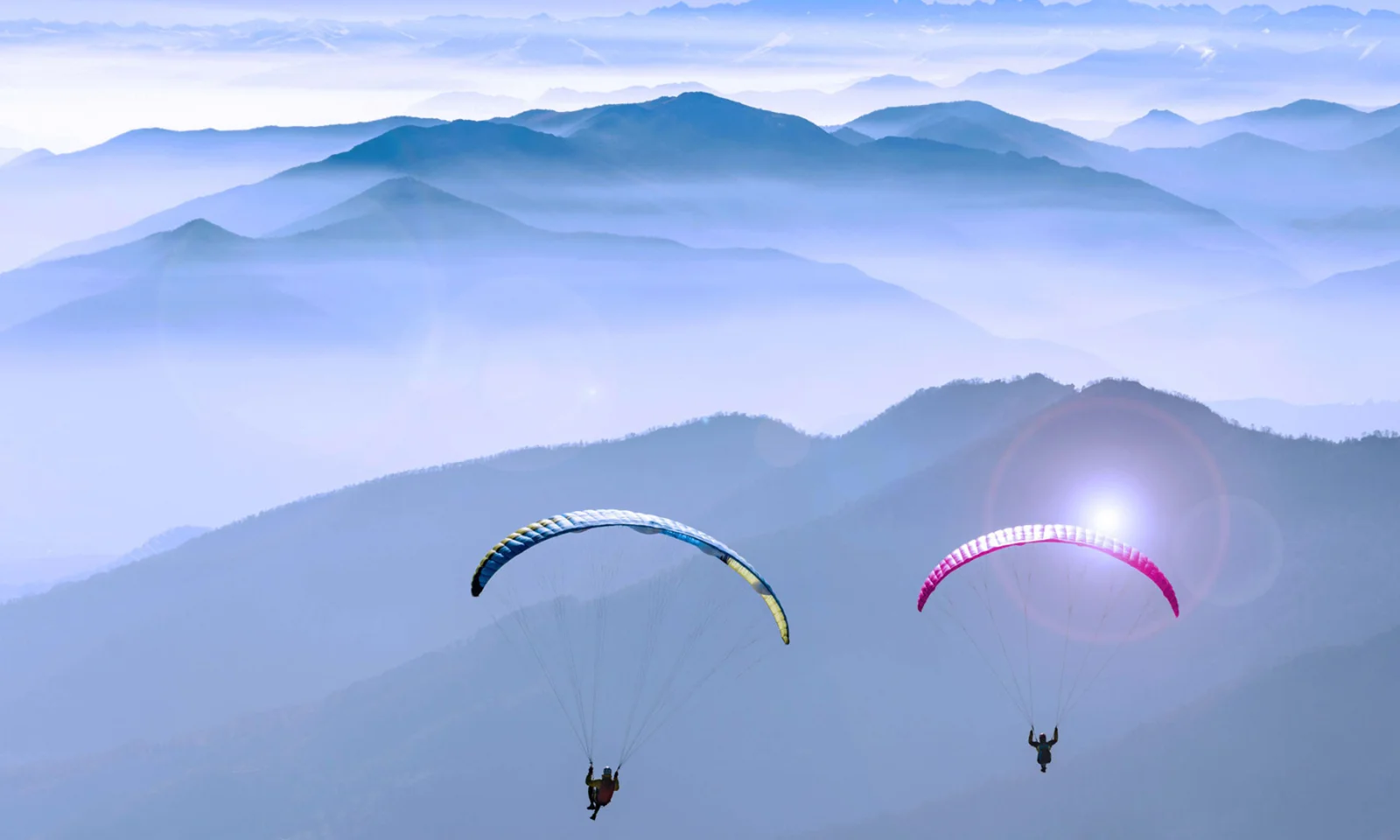 Uma imagem inspiradora de dois parapentes voando sobre cadeias de montanhas, representando a transição segura e perfeita para a tecnologia de nuvem. Este visual reflete a jornada do Honda Bank na aceleração da transformação digital por meio de uma zona de pouso segura na nuvem, com a expertise da GFT garantindo um processo de migração tranquilo e seguro.