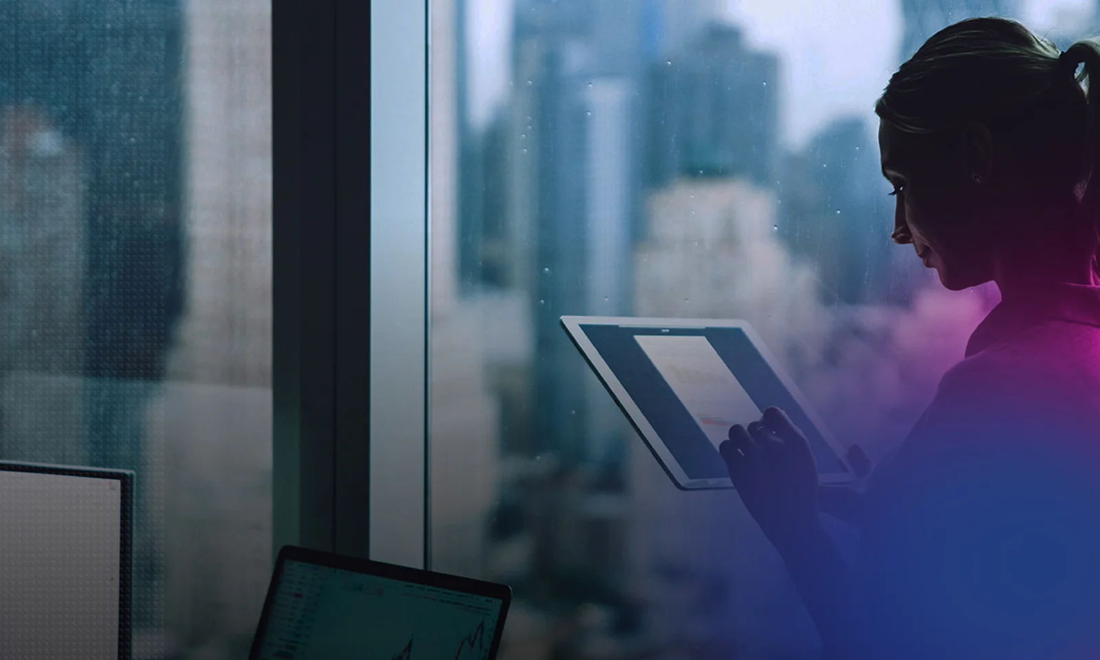 A businesswoman standing by a window, using a tablet to analyze data, with city skyscrapers blurred in the background.