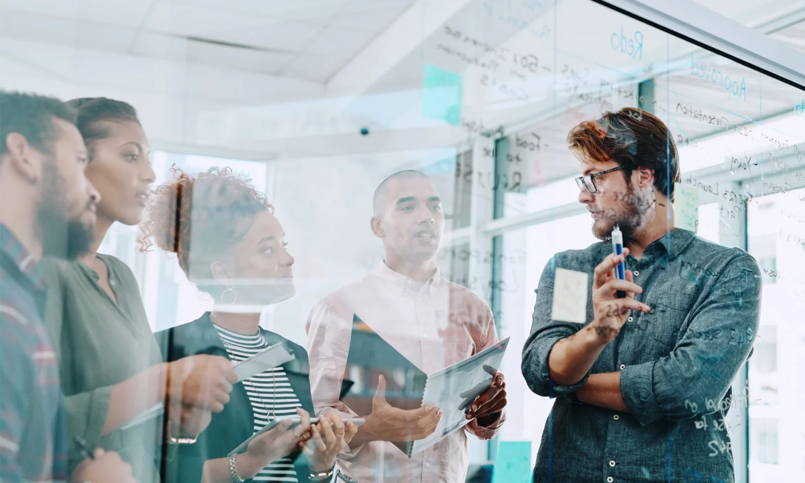 A group of diverse professionals collaborating and brainstorming ideas on a glass board in a modern office setting