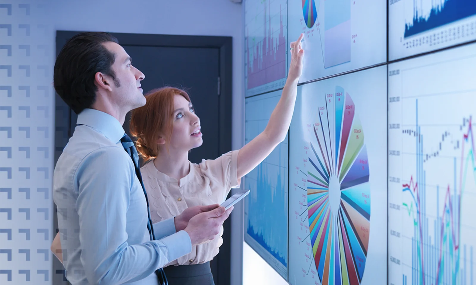 Two business analysts examining large digital screens displaying complex data visualizations, graphs, and charts, focused on analyzing trends.