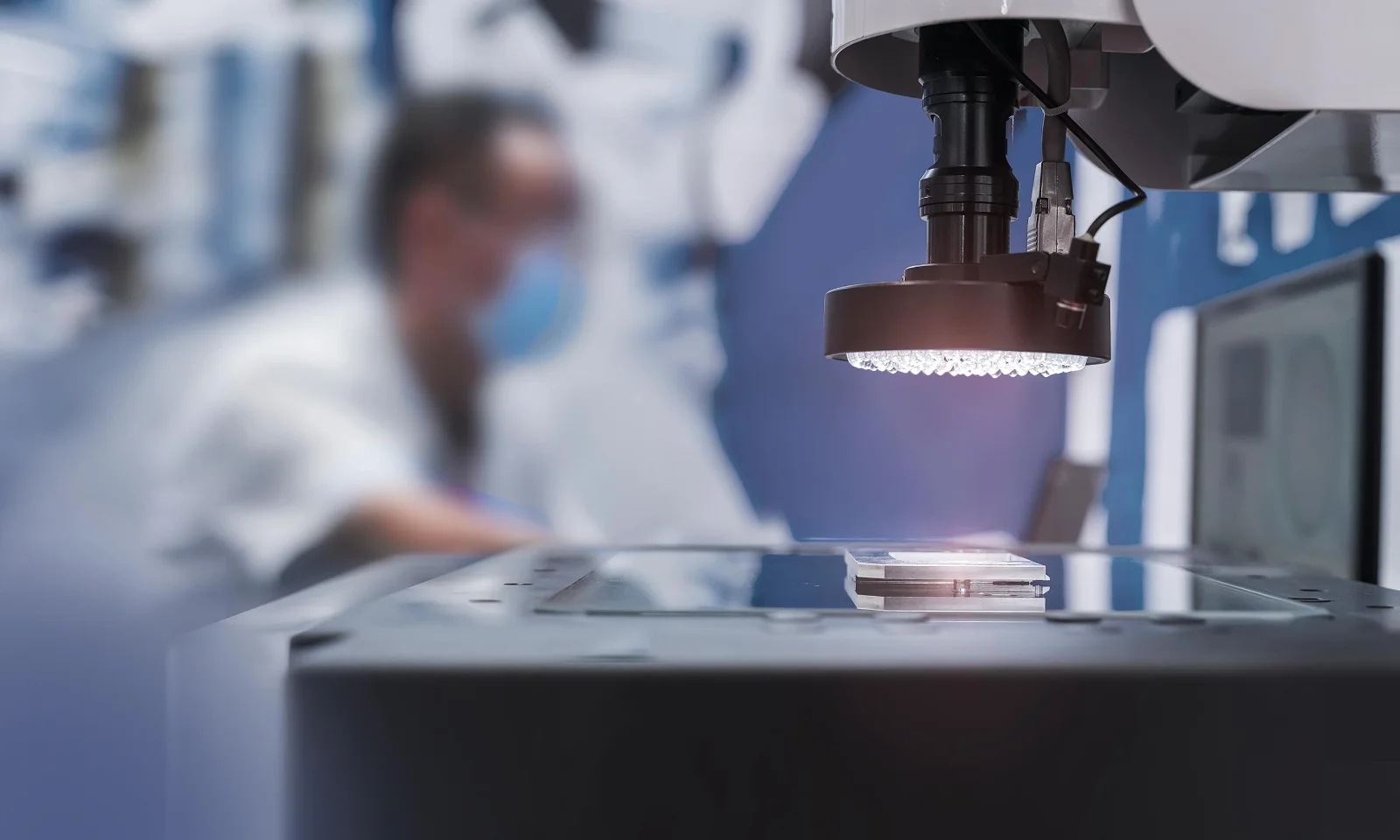 Close-up of a high-tech visual inspection system with a blurred technician in the background, emphasizing precision and advanced technology.