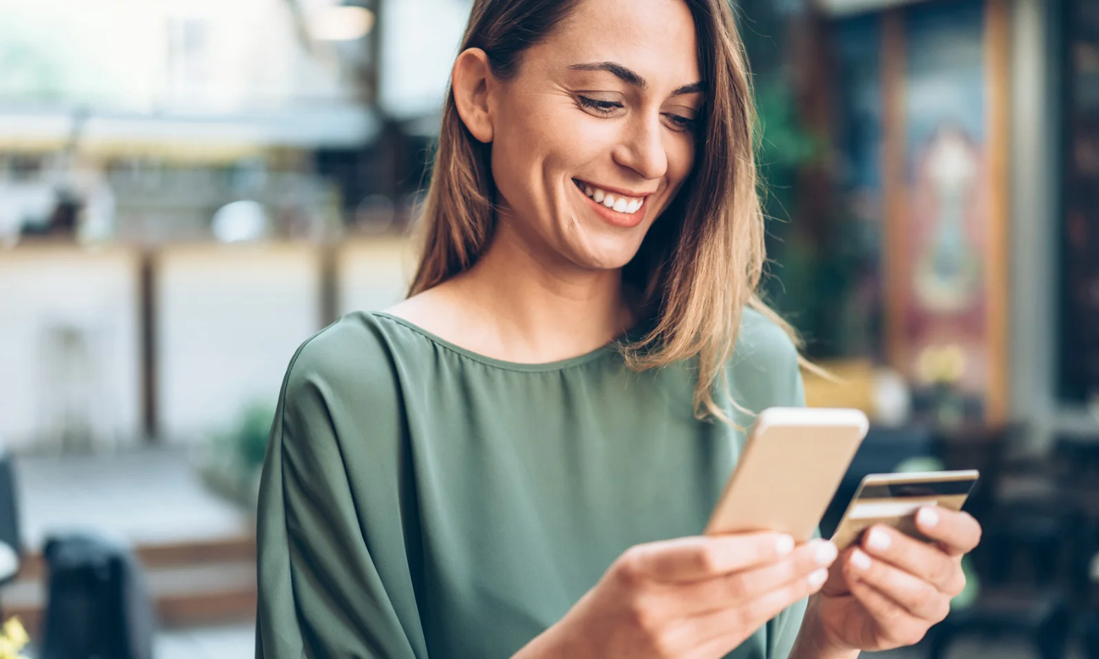 A smiling woman using a smartphone and holding a credit card, representing the convenience of a new business banking mobile app.