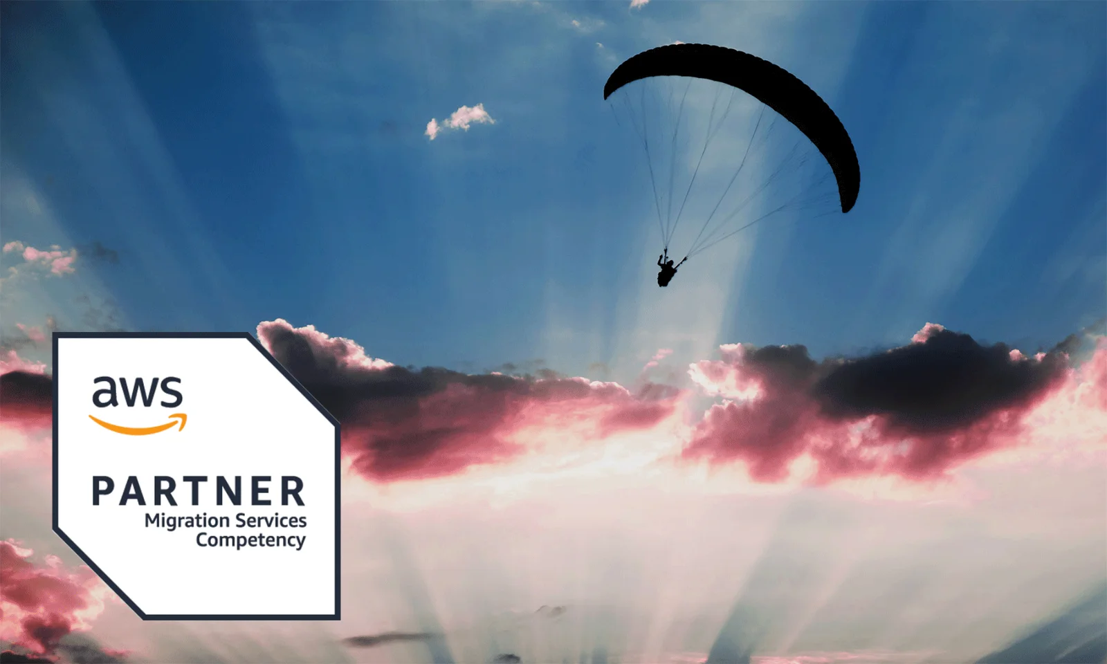 A visual representation of cloud migration featuring a silhouette of a paraglider soaring through a sky with vibrant clouds and sunrays. The AWS Partner Competency badge for Migration Services is displayed in the lower left corner, signifying certified expertise in cloud migration.