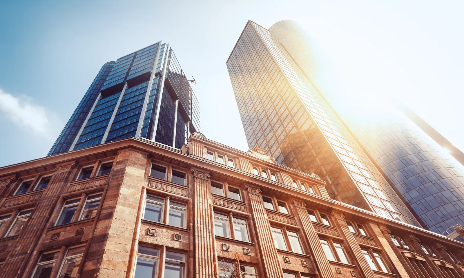 Hohes Gebäude aus der Froschperspektive mit strahlender Sonne und blauem Himmel im Hintergrund, dargestellt als Key Visual für Finanzdienstleistungen.