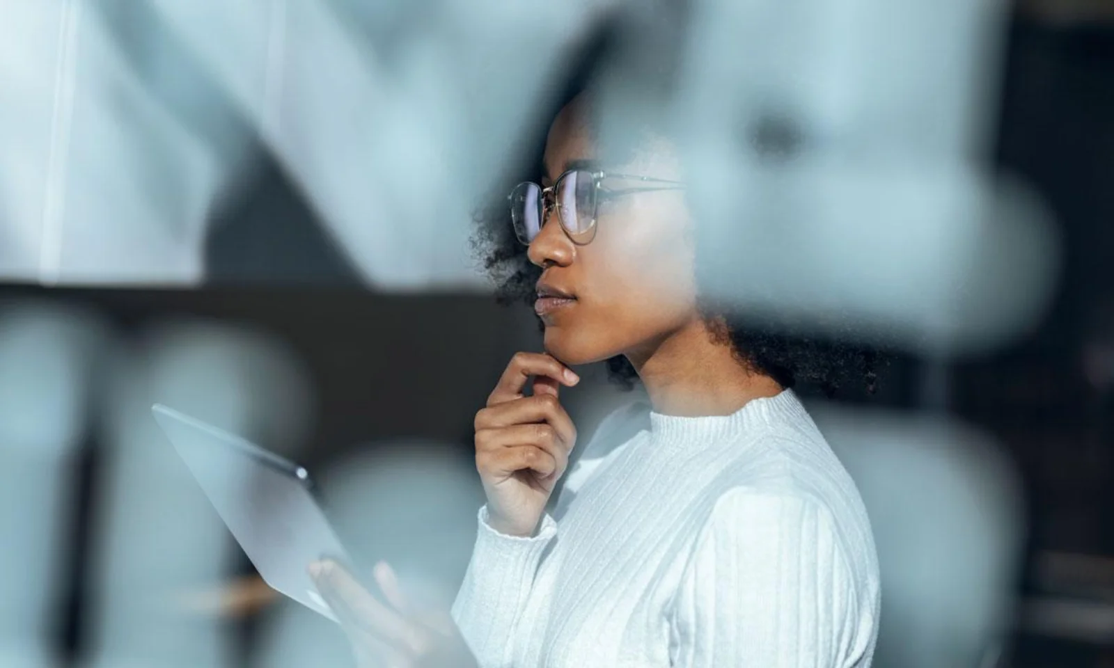 A woman wearing glasses, deep in thought while reviewing data on a tablet, symbolizing analysis and strategic thinking.