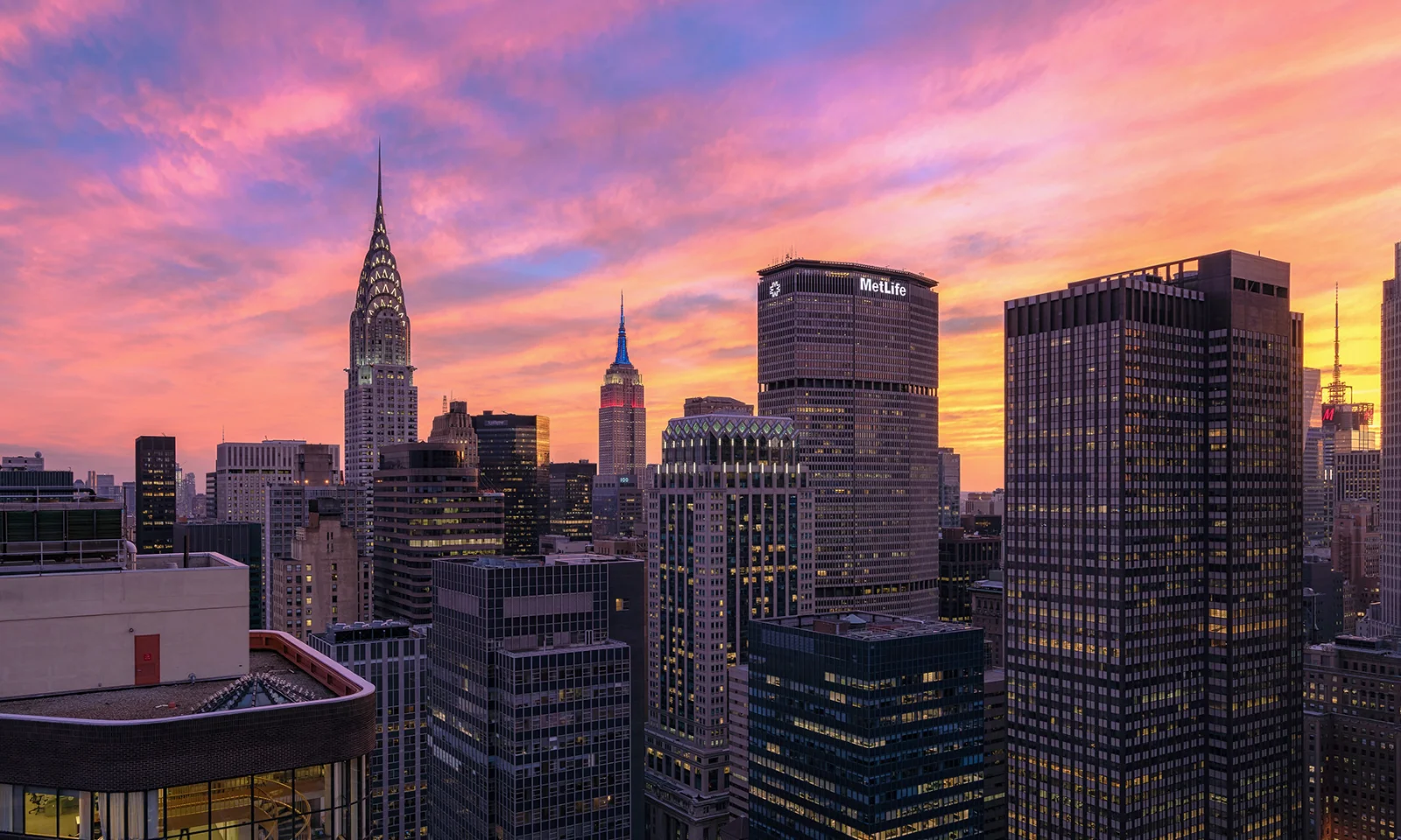 A vibrant sunset over the New York City skyline, featuring iconic skyscrapers such as the Chrysler Building and the MetLife Tower.