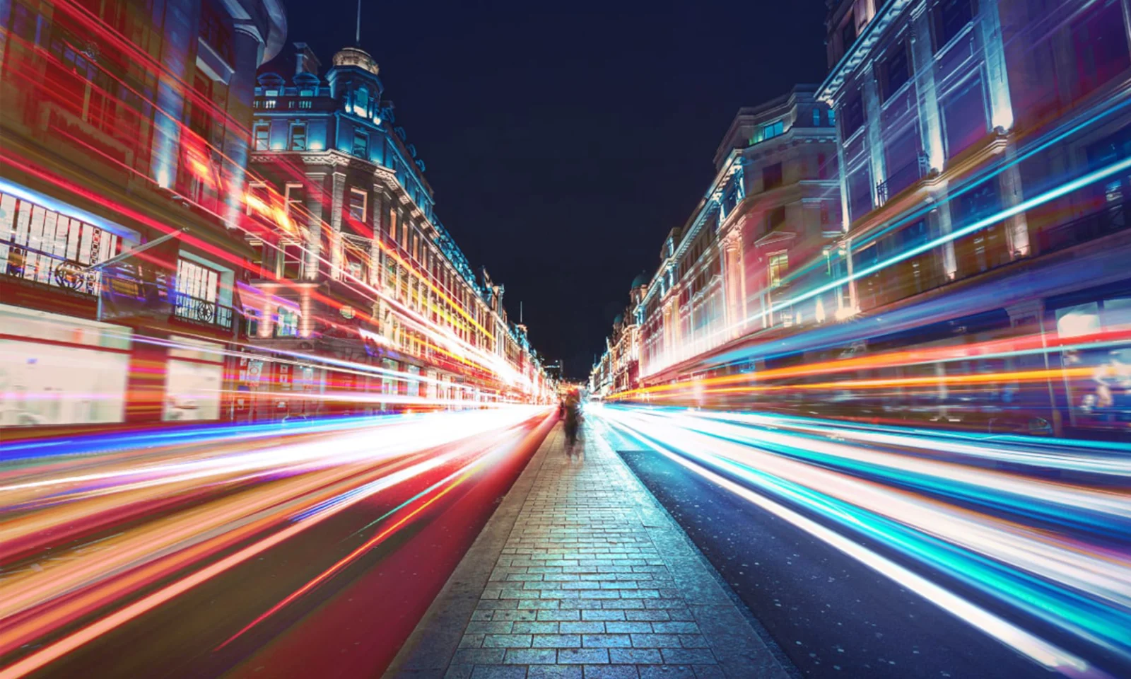 A vibrant city street at night, illuminated by streaks of colorful lights, representing the fast-paced and dynamic nature of modern banking and finance.