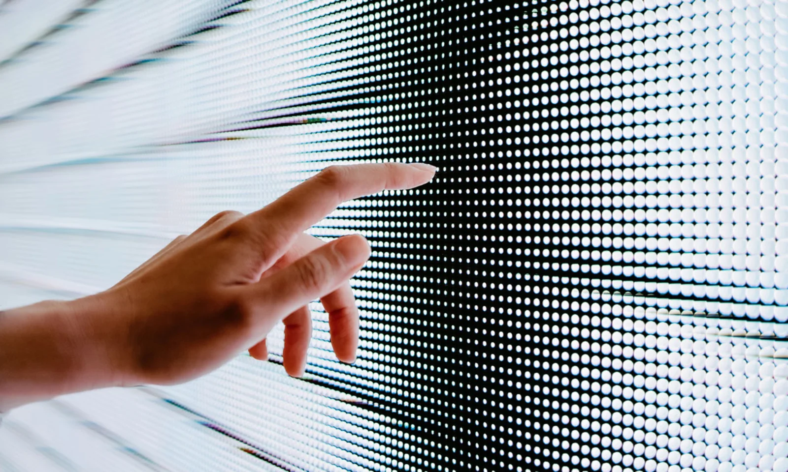 Close-up of a hand reaching out to interact with a digital interface made of illuminated dots, symbolizing advanced technology and human-computer interaction.