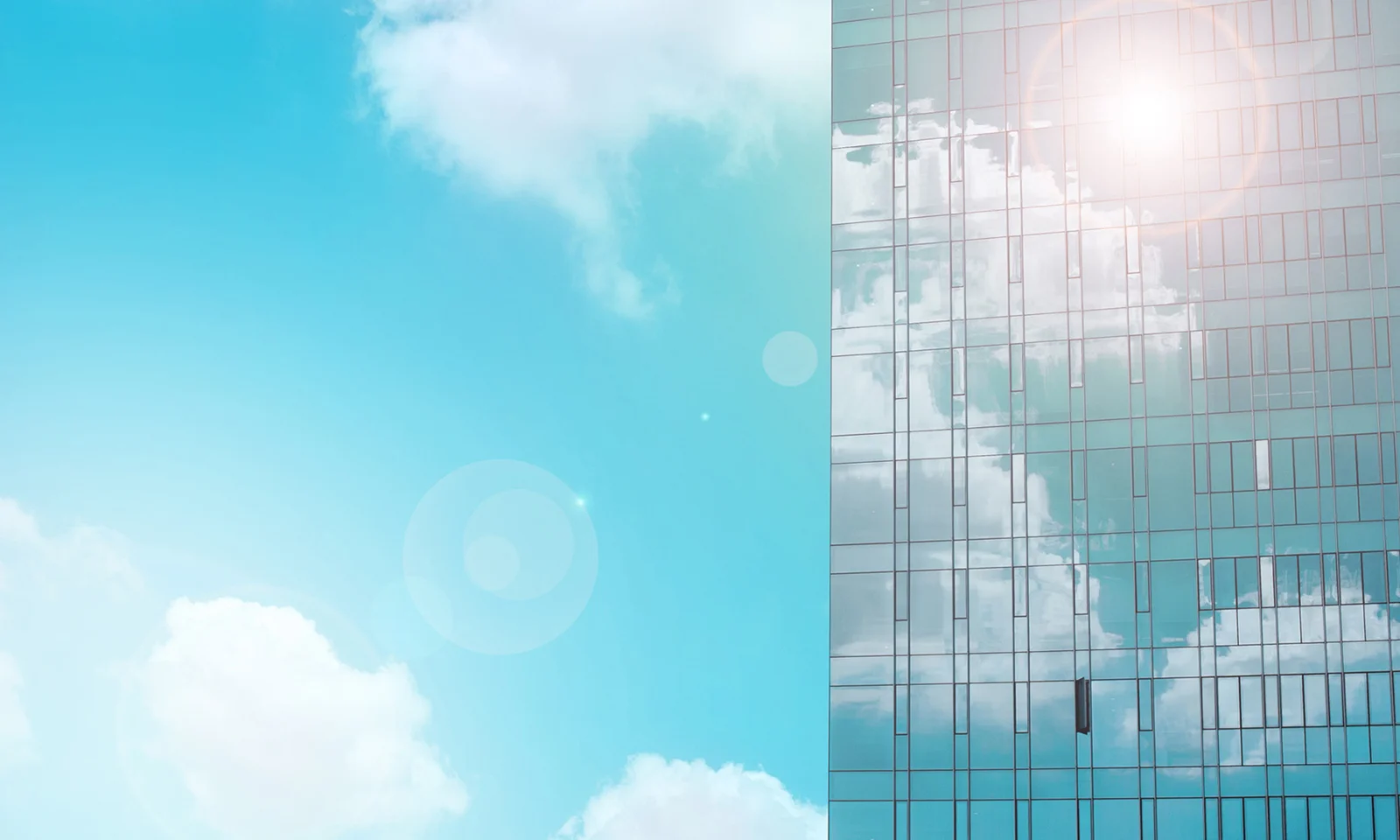 A modern glass skyscraper reflecting a bright blue sky with soft white clouds, symbolising innovation and growth.