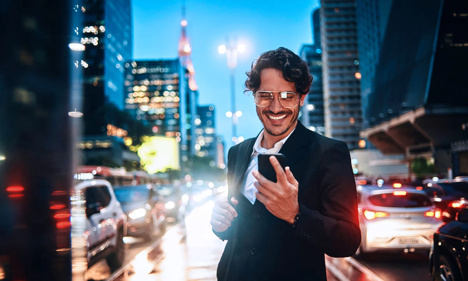 A smiling business professional interacts with a smartphone in a bustling city at night, symbolising the future of digital banking.