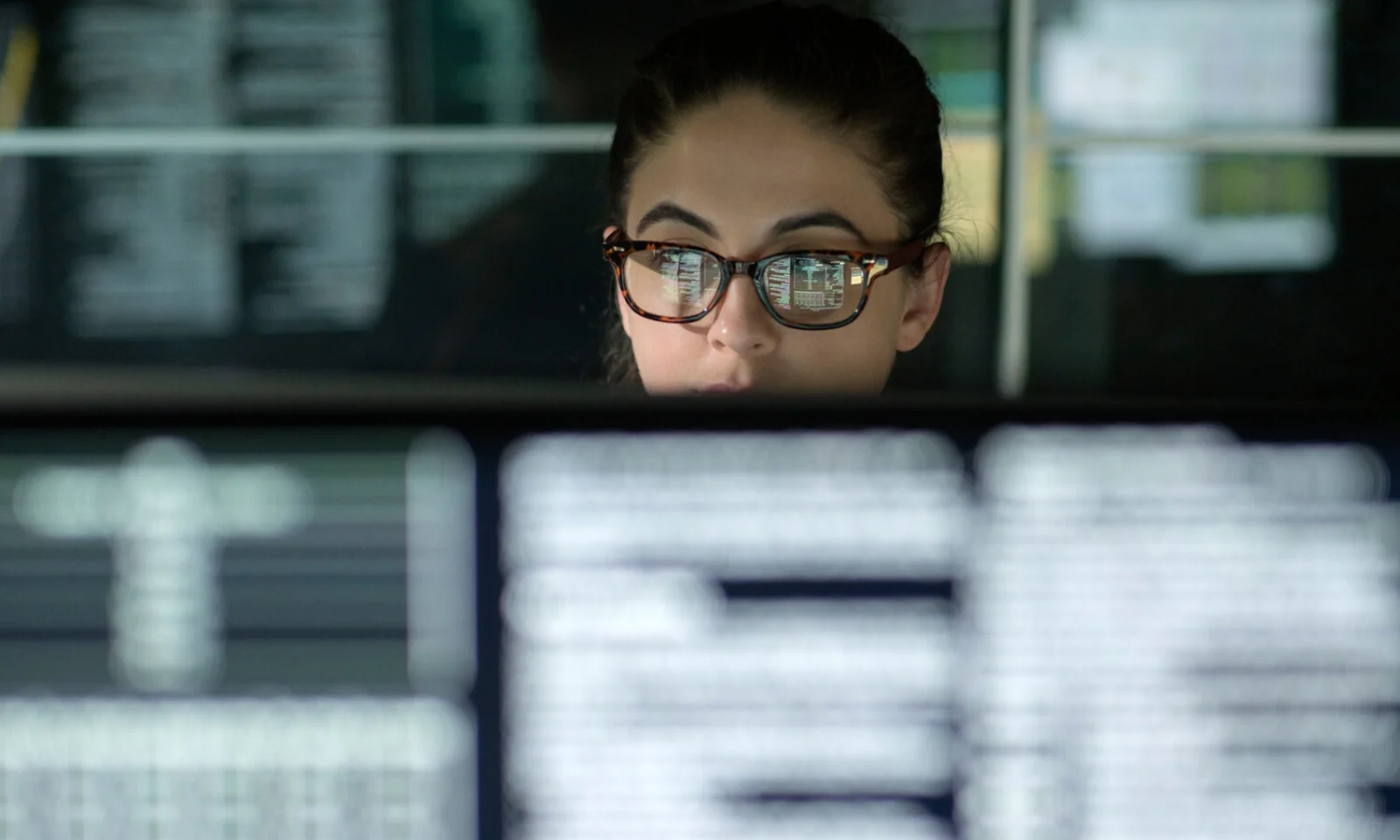 A person wearing glasses with computer code reflected on the lenses, sitting in front of multiple screens filled with lines of code, representing the technical and innovative environment of AWS Windows.