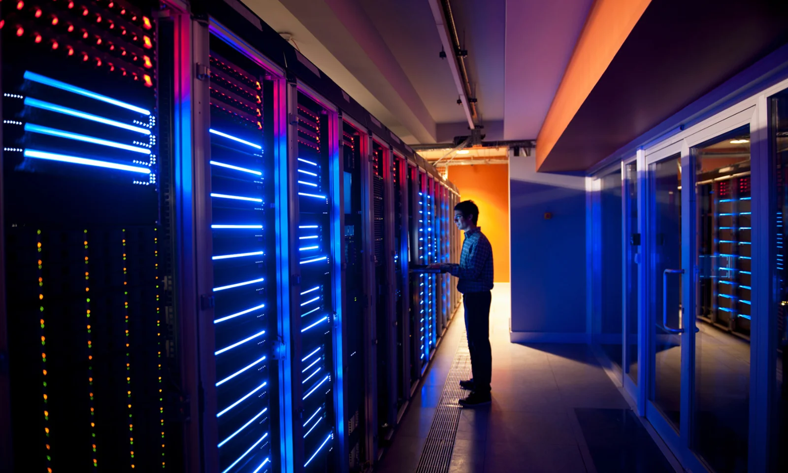 Technician working in a data centre with blue and red illuminated servers