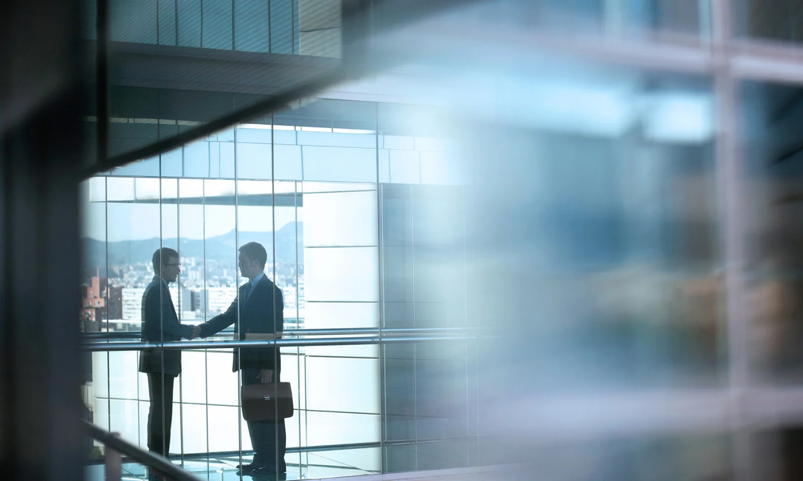 Two business professionals shaking hands in a modern office building with a cityscape in the background