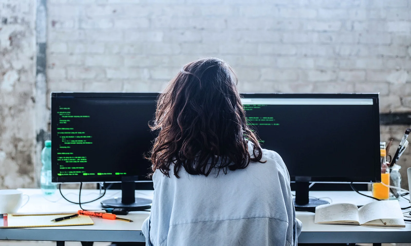 A young professional working at a dual-monitor setup in an industrial-style office, representing the growth of tech talents