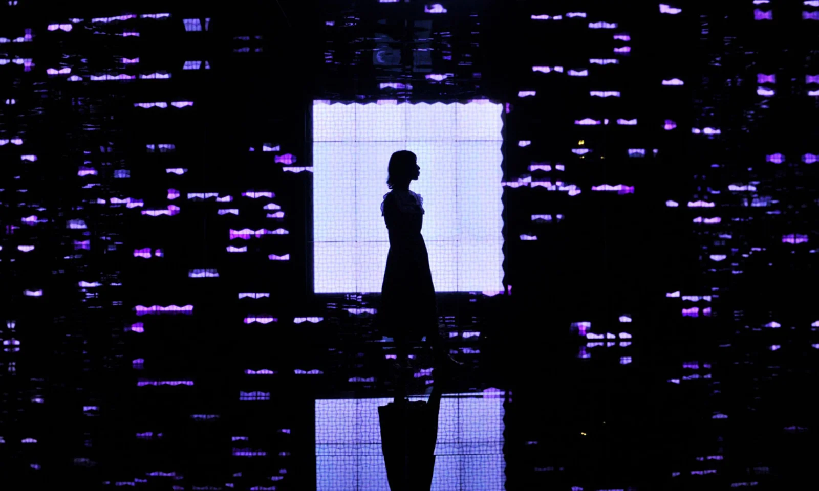 Silhouette of a woman standing in front of a bright screen, surrounded by digital patterns of purple light, symbolizing the intersection of technology and human presence.