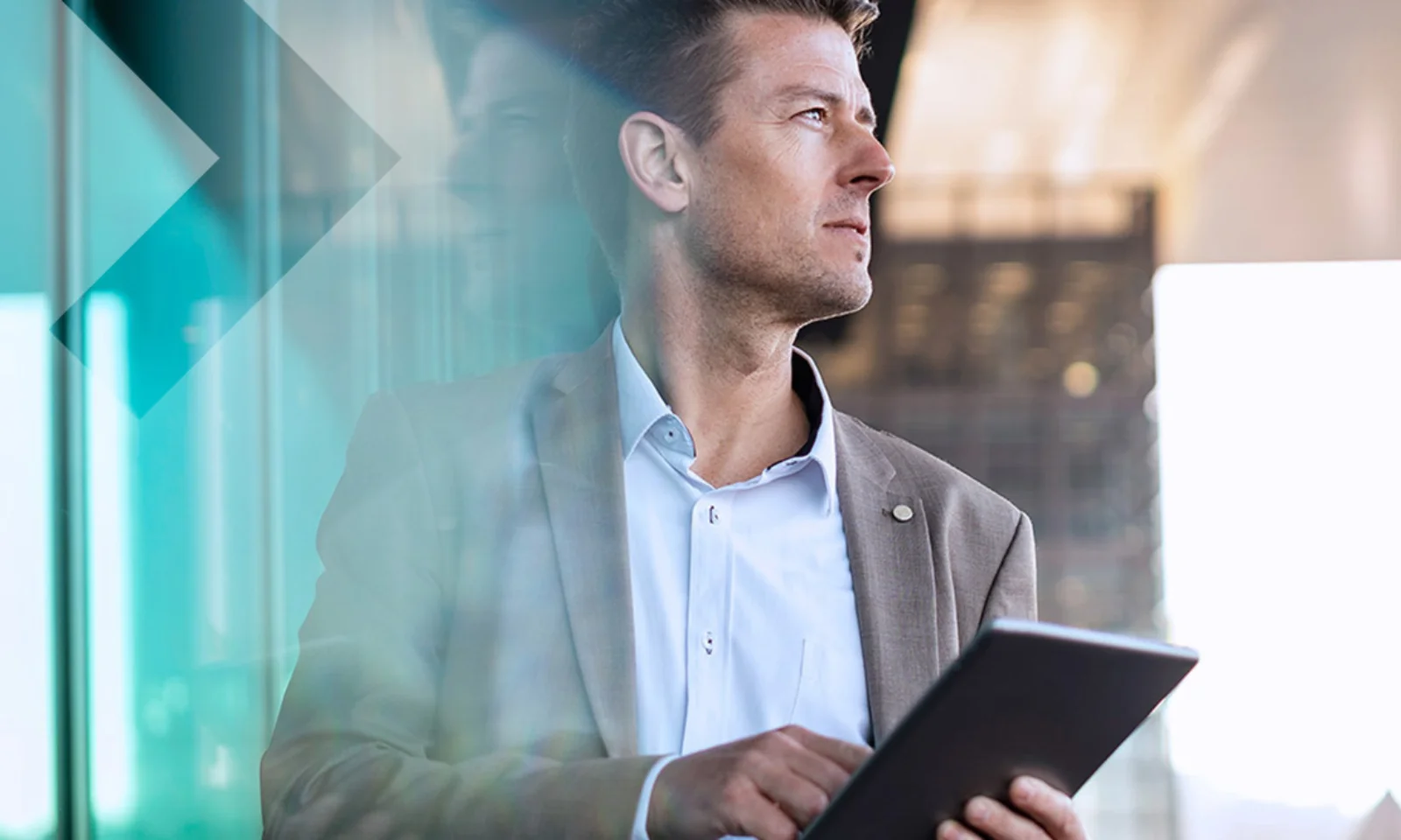 A business professional holding a tablet and looking thoughtfully out of a window, symbolizing strategic planning and modern technology in a corporate setting.