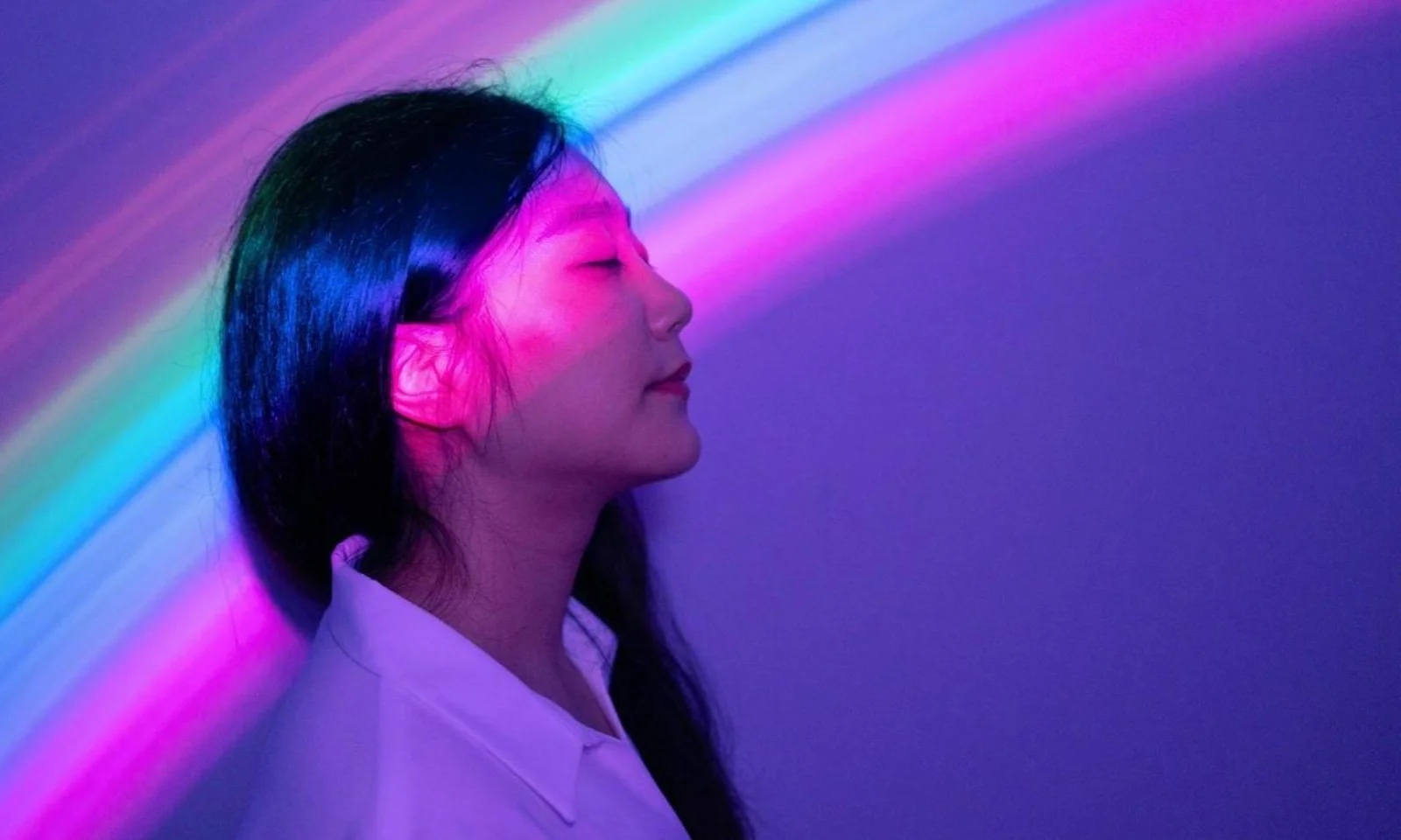 A serene woman with closed eyes bathed in vibrant, multi-colored light beams, symbolizing the diverse and integrated services offered.