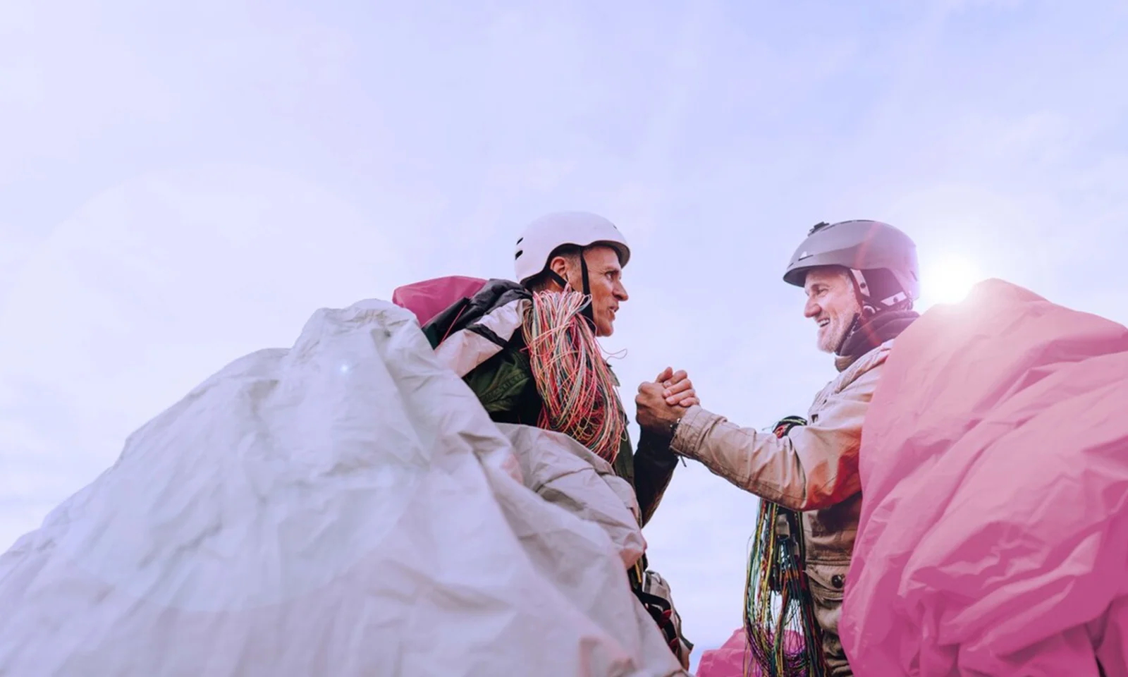 Two paragliders shaking hands, ready for their adventure, with parachutes spread around them.