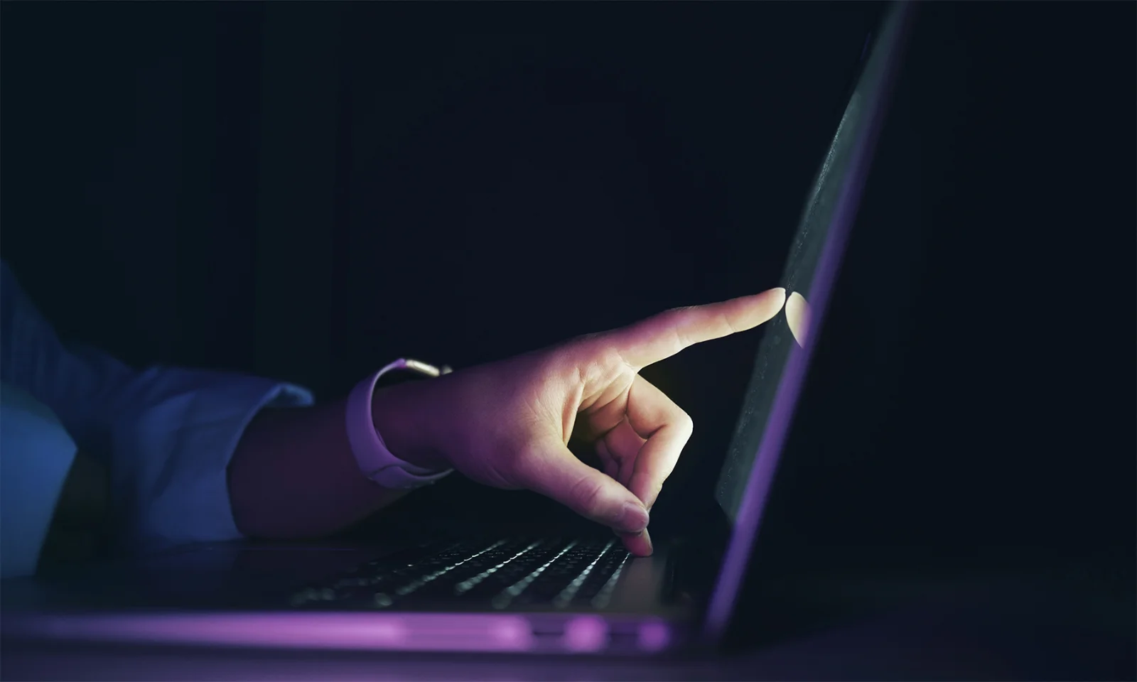 A close-up of a hand interacting with a laptop touchscreen in a dimly lit environment, representing seamless user experience and digital responsiveness.