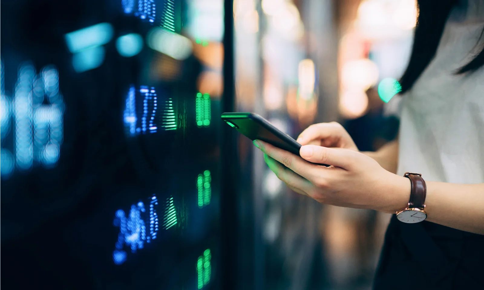 Close-up of hands holding a smartphone in front of a digital screen displaying financial data, representing the concept of green bonds and sustainable finance.