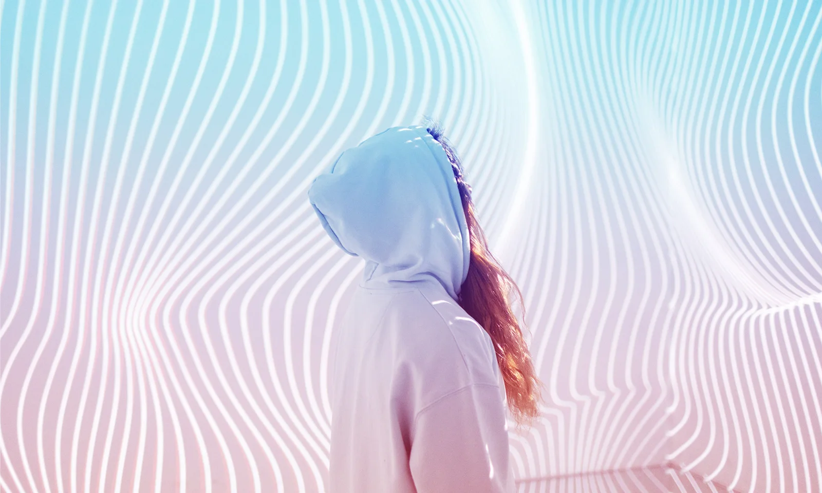 A person in a hooded sweatshirt standing in front of a modern, abstract background with flowing lines and vibrant colours, symbolising the innovative transformation in the insurance industry through mainframe modernisation.