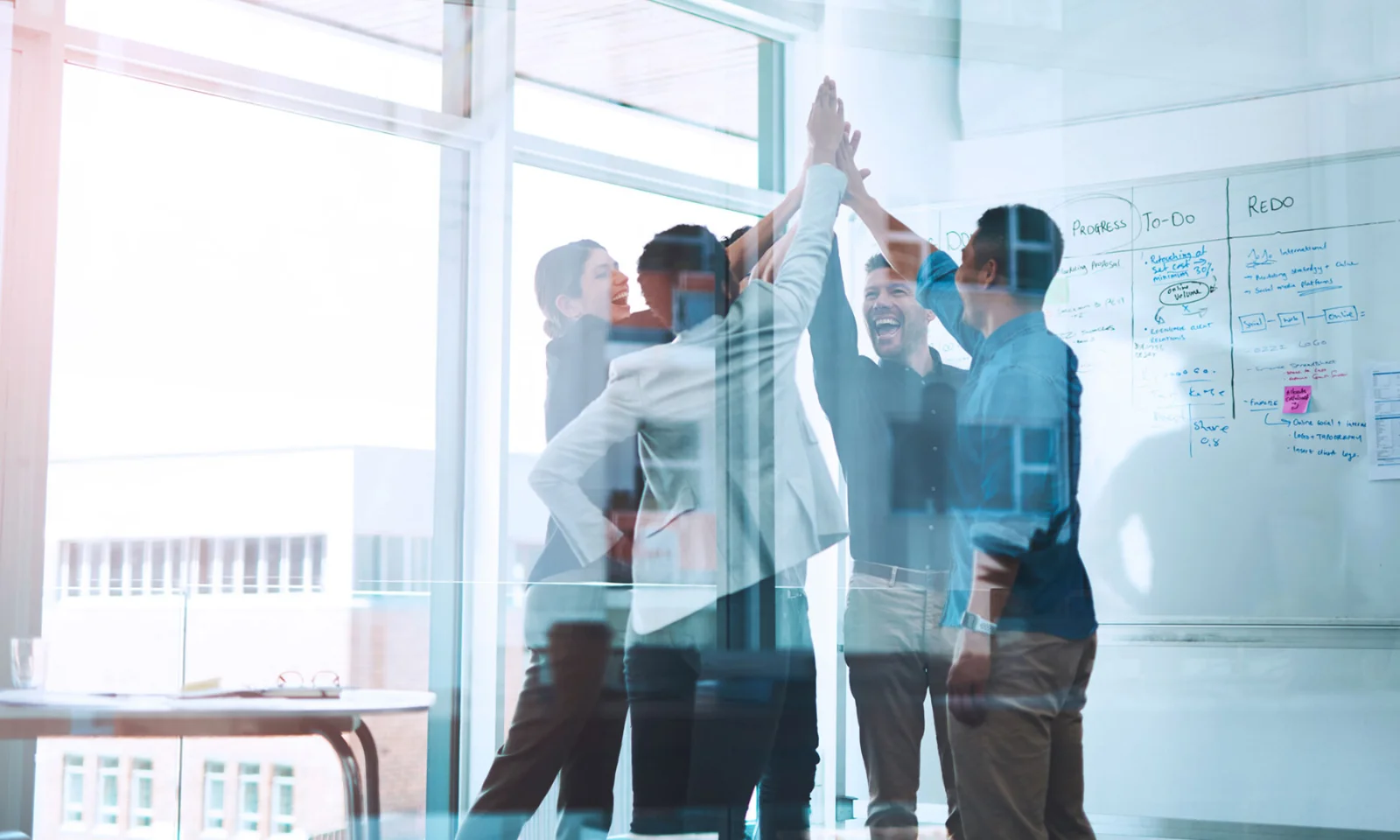 A team of professionals celebrating a successful project in a bright, modern office space, with a whiteboard in the background showcasing project plans and progress.