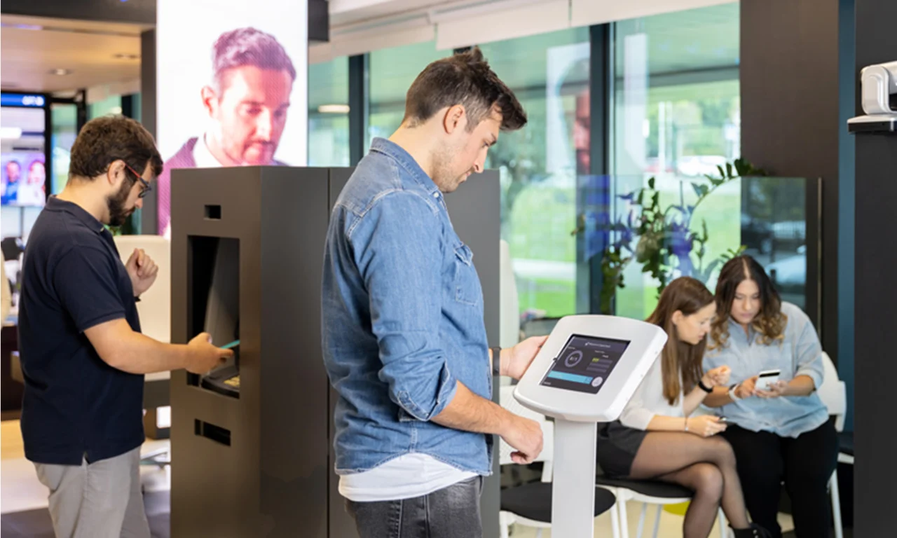 People interacting with digital kiosks and devices in a modern bank branch, highlighting innovative banking solutions and customer engagement technologies.